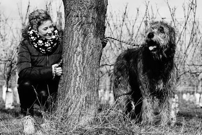 Happy woman playing with irish wolfhound by tree at forest