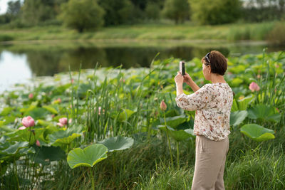 Rear view of senior woman taking a picture by lotuses lake