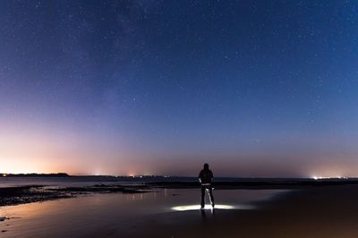 Rear view of man standing at beach against star field