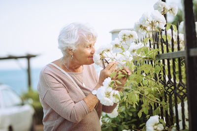 Elderly woman admiring beautiful bushes with white roses