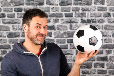 Portrait of young man holding ball while sitting on stone wall