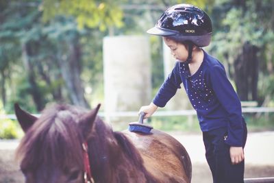 Side view of cute girl cleaning horse with brush at farm