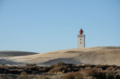 Lighthouse on street amidst buildings against clear sky