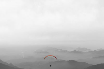 Person paragliding over mountains against sky