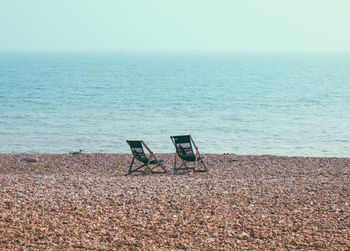 Deck chairs on beach against clear sky