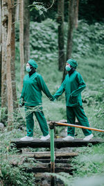 Doctors wearing mask holding hands while standing in forest