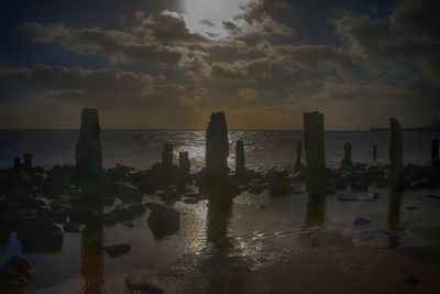 Wooden posts on beach against sky during sunset