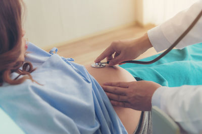 Cropped hands of doctor examining pregnant woman belly with stethoscope in clinic