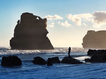 Silhouette person standing on rock in sea against sky