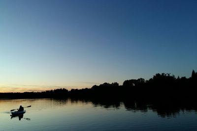 Silhouette person sailing boat in lake against sky