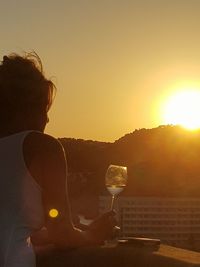 Rear view of woman drinking glass at sunset