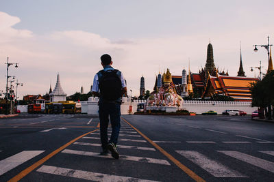 Rear view full length of man walking by temple on road in city