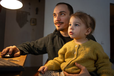 Father using computer while daughter looking at it