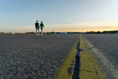 People walking on road against sky during sunset