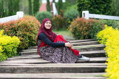 Woman looking away while sitting on wood by plants