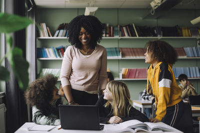 Smiling teacher interacting with students while doing e-learning in classroom