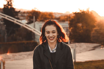 Smiling young woman looking away while standing outdoors during sunset