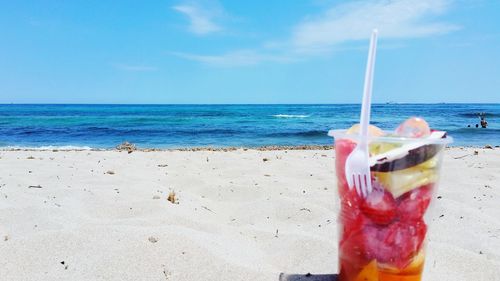 Fruits in disposable cup at beach against sky