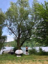 Woman standing by tree on field by lake