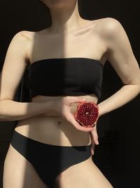 Midsection of woman holding pomegranate while standing against black background