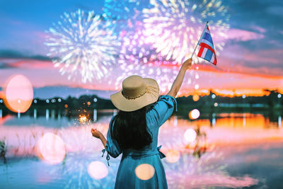 Rear view of woman with umbrella against illuminated sky