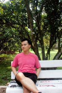 Full length of young man sitting against trees