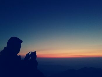 Silhouette man photographing at sunset