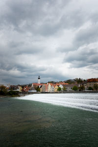 View of city at waterfront against cloudy sky