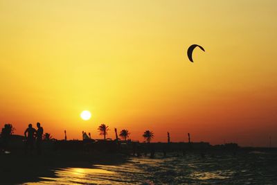 Silhouette parachute flying over beach against sky during sunset