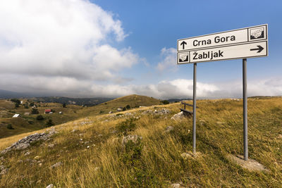 Road sign on field against sky