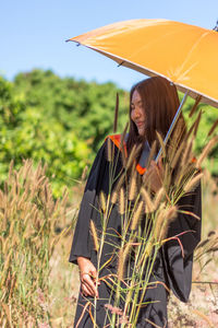 Smiling young woman with umbrella standing on field 