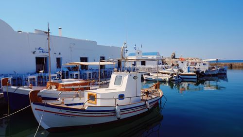 Boats moored at harbor against clear blue sky