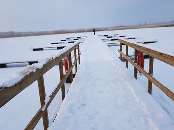 Snow covered wooden posts in frozen lake against sky