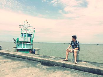 Man sitting on bollard against sea