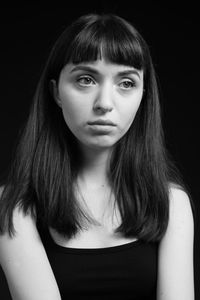 Close-up of young woman looking away while sitting against black background