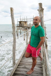 Full length of bald man leaning on pier railing over sea