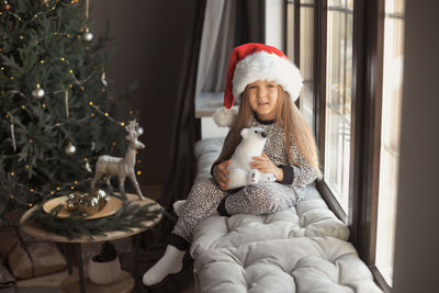 Portrait of girl with stuffed toy sitting by window