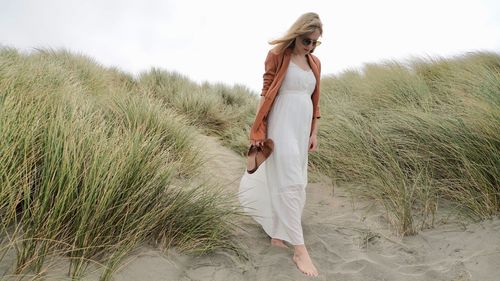 Young woman standing on sand at beach against sky