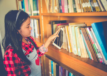 Girl keeping digital tablet in bookshelf