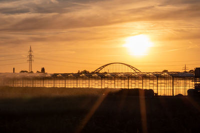 Silhouette bridge over river against sky during sunset