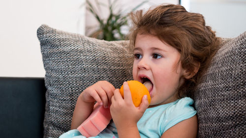 Close-up of girl eating fruit while lying on sofa