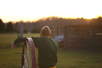Rear view of young man standing on field against sky during sunset