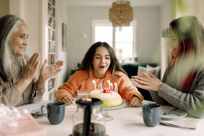 Cheerful girl celebrating birthday with mother and grandmother at home