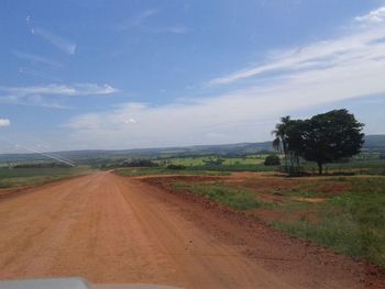 Road passing through field against cloudy sky