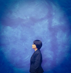 Side view of businesswoman standing against blue wall