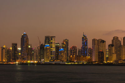 Illuminated buildings by sea against sky at night