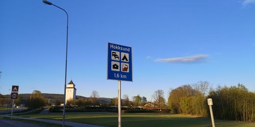 Road sign by street against clear blue sky