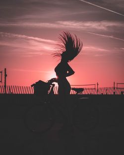 Silhouette woman with tousled hair standing against sky during sunset
