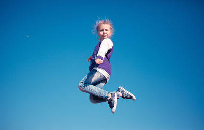 Low angle portrait of girl jumping against clear blue sky