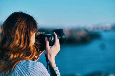 Rear view of woman photographing against sea